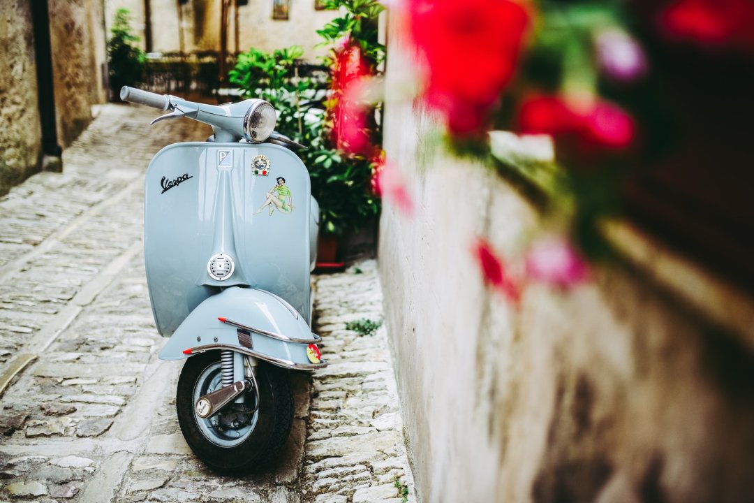 Marque de scooter Vespa bleu garé dans la ruelle d’un village