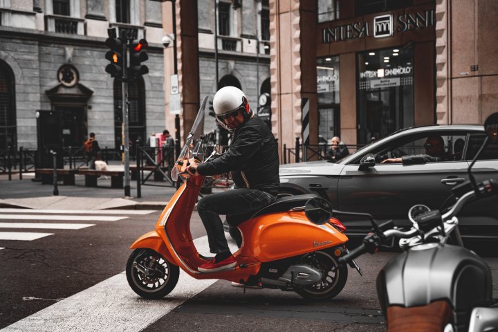 Marque de scooter Vespa orange conduit par un homme en centre-ville